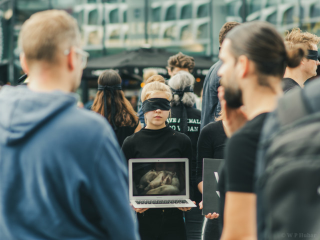 Een outreacher en voorbijganger kijken naar de beelden vanuit de Save Square